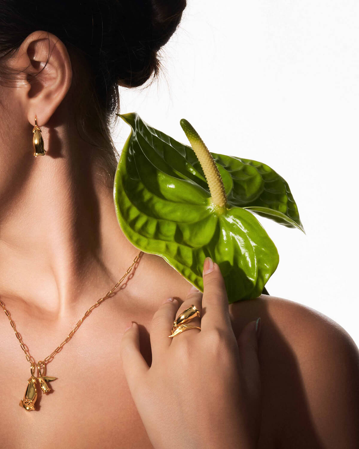 a woman holding a green leaf and wearing gold jewelry