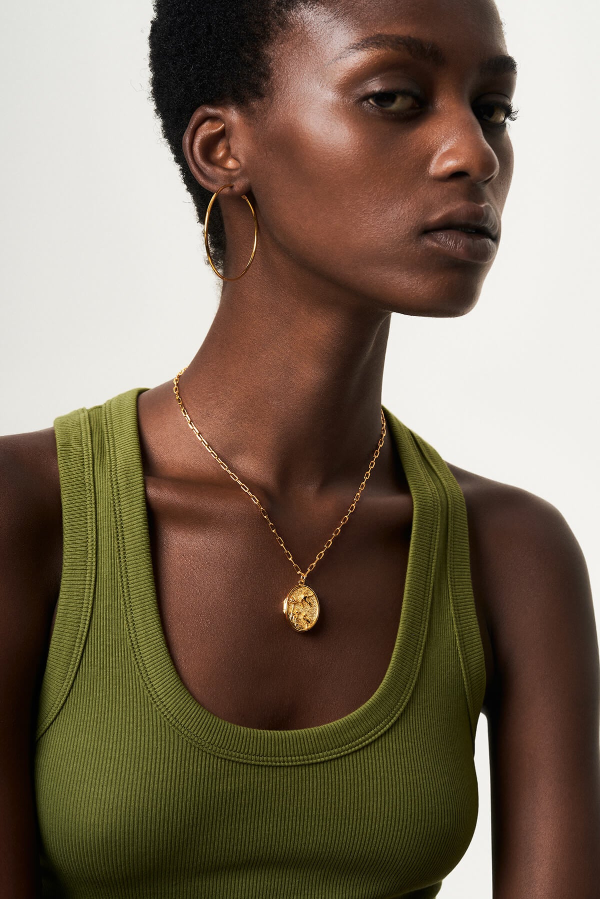 a woman wearing a green tank top and gold earrings