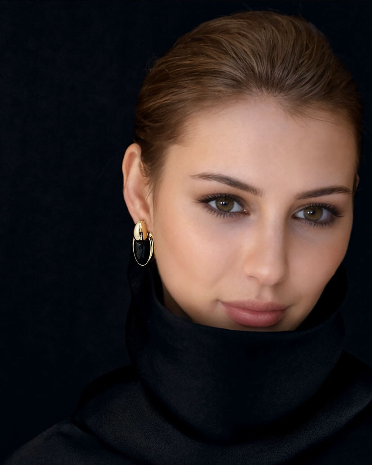 a woman wearing a black turtle neck and gold hoop earrings