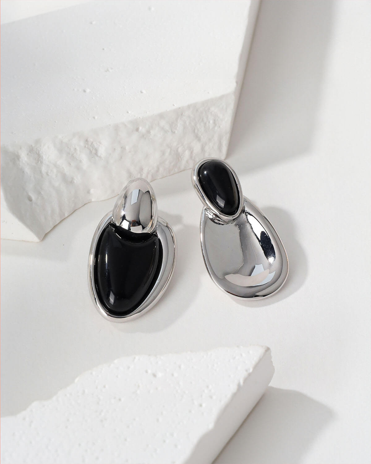 a pair of black and silver earrings on a white surface