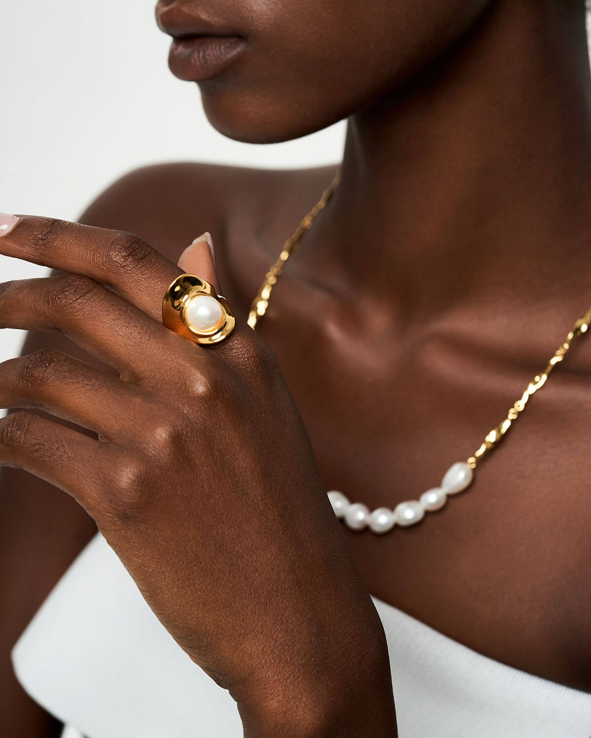 a woman wearing a pearl necklace and a gold ring