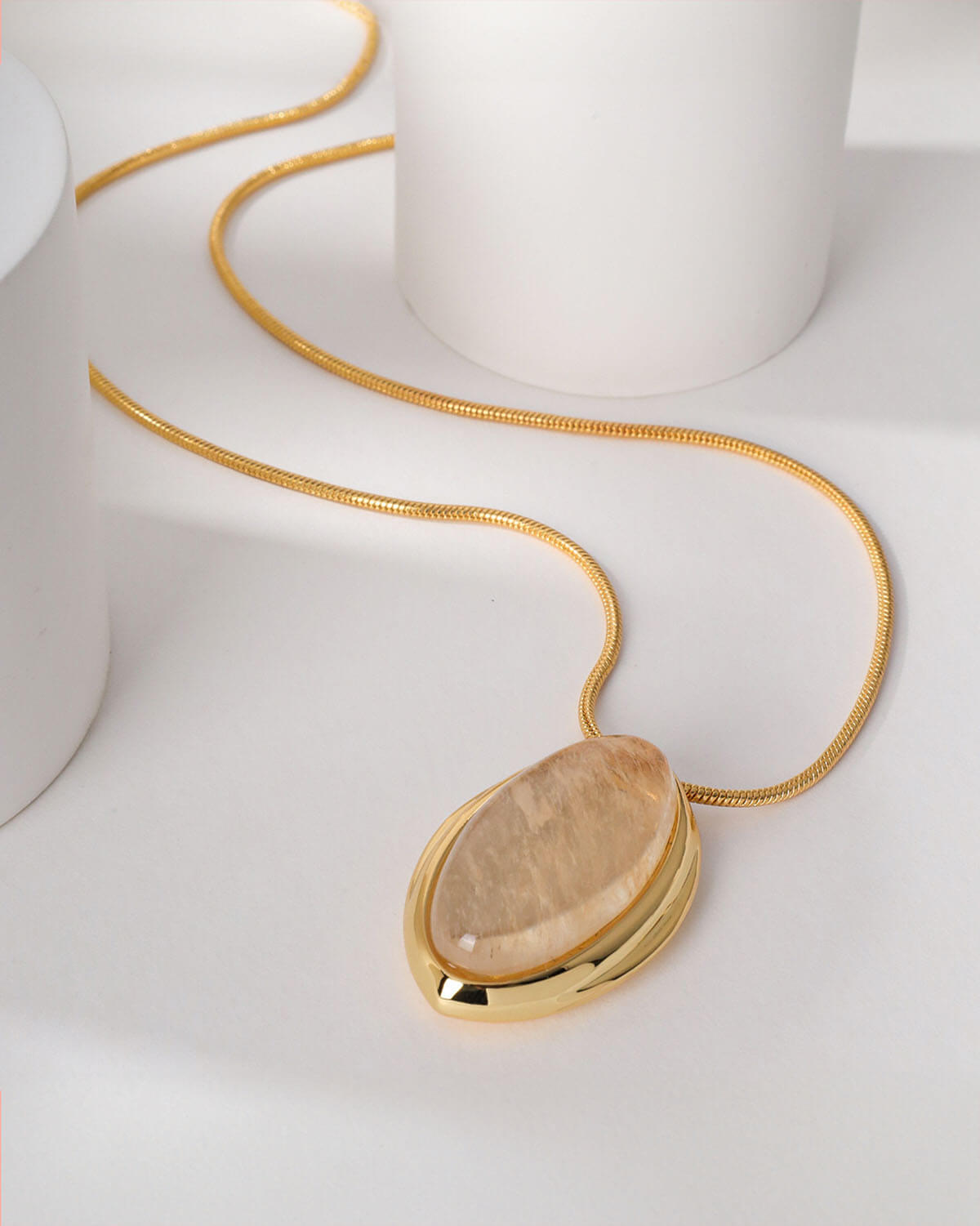 a gold necklace with a brown stone on a white surface