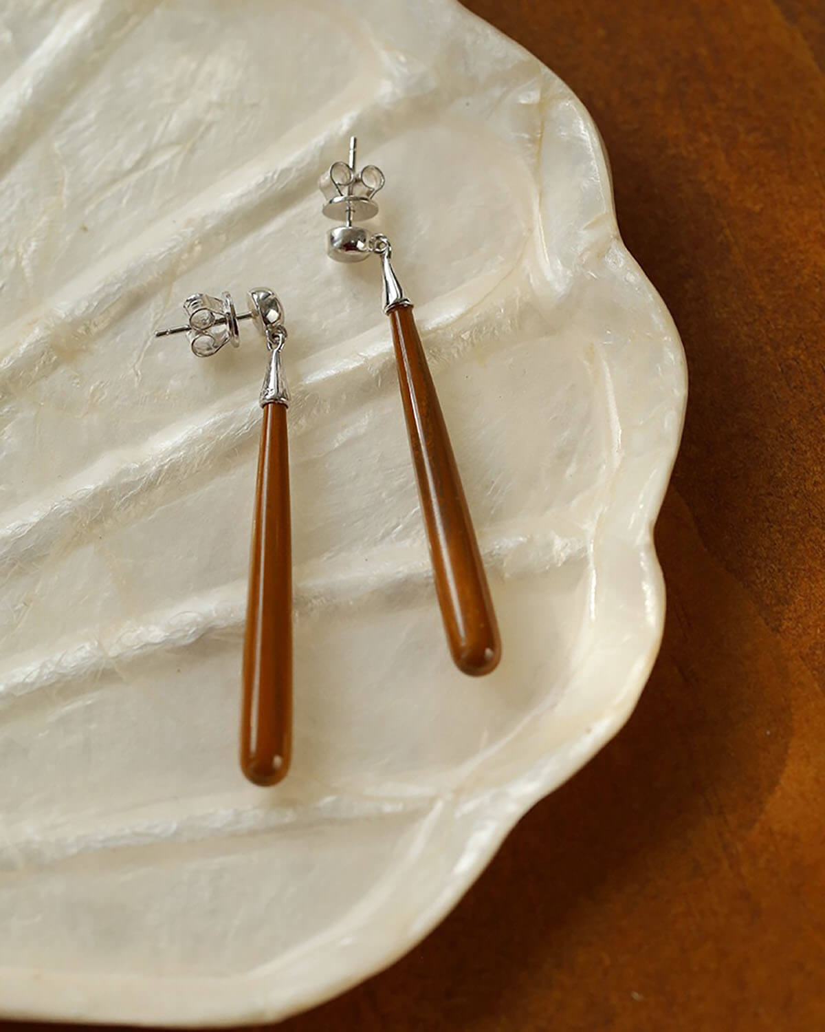 a pair of brown and silver earrings sitting on top of a white shell